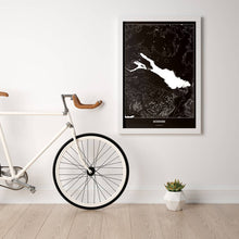 Lade das Bild in den Galerie-Viewer, Bodensee Dark Poster - Minimal - Vorschau in einem hellen Zimmer mit Fahrrad an Wand angelehnt

