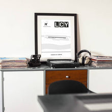 Lade das Bild in den Galerie-Viewer, London City Airport (Flughafen LCY / EGLC) Light Poster - Minimal - Vorschau auf einem Tisch mit Plattenspieler und Kamera