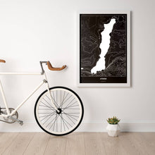 Lade das Bild in den Galerie-Viewer, Attersee Dark Poster - Minimal - Vorschau in einem hellen Zimmer mit Fahrrad an Wand angelehnt
